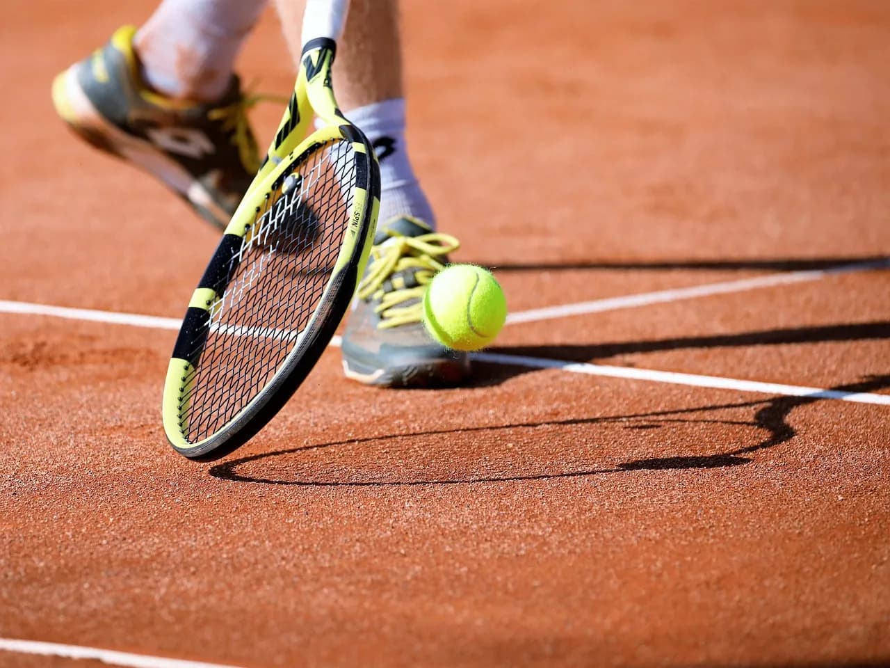 A tennis racket hitting a ball on a clay court