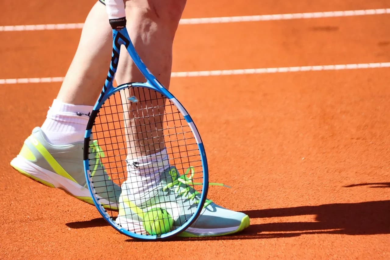 A tennis player's feet and racket on a clay court