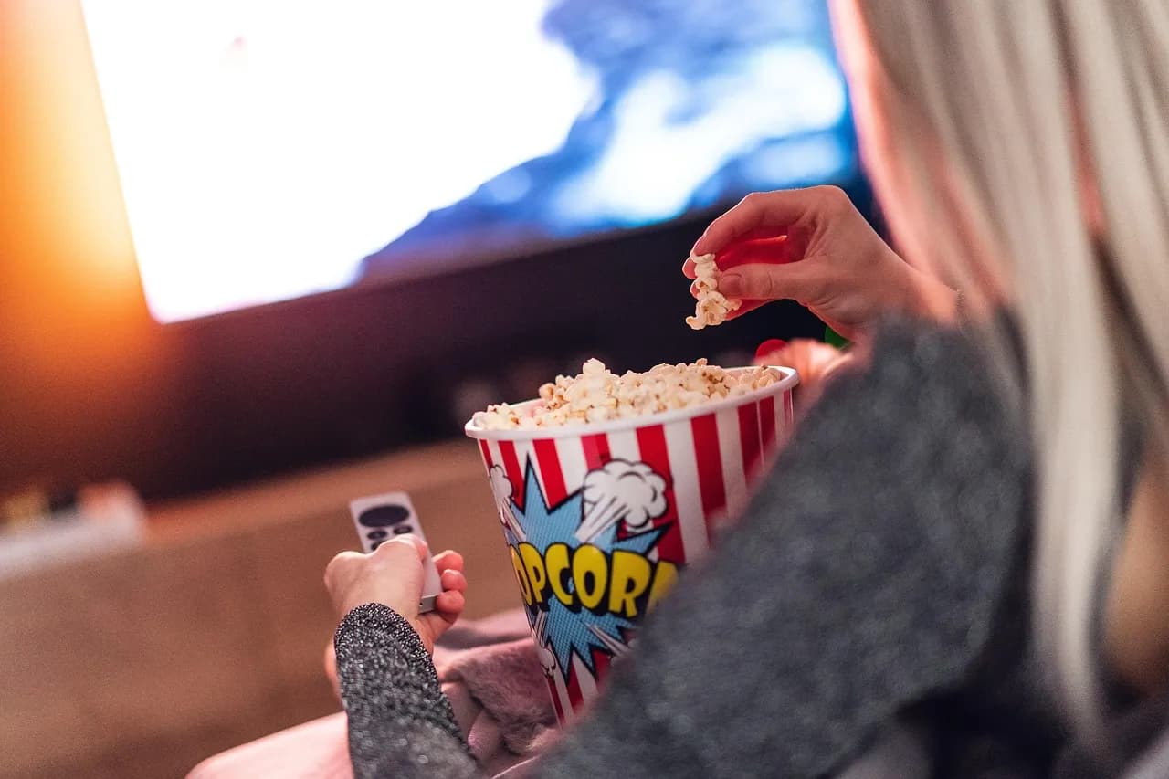 A woman eating popcorn while watching TV at home